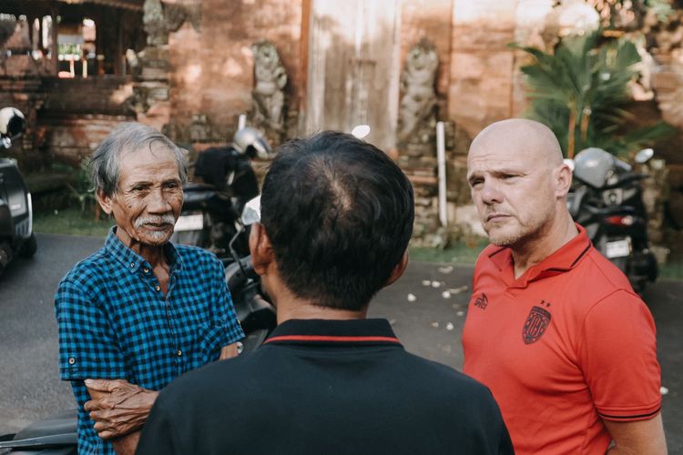 Pelatih Bali United Johnny Jansen berdialog dengan warga disela-sela aksi sosial memberikan bantuan kepada korban banjir di Posko Pengungsian Banjar Tohpati, Desa Kesiman Kertalangu, Denpasar Timur, Kamis (11/9/2025) sore.