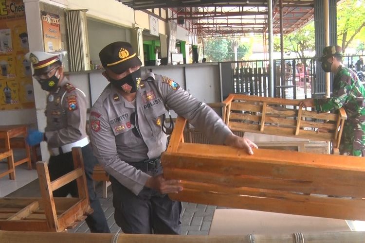 Petugas gabungan di Trenggalek Jawa Timur, menaikkan kursi di atas meja, agar tidak digunakan duduk oleh warga. Warung tidak boleh melayani pembeli yang makan di tempat, ppkm diperpanjang sampai tanggal berapa Selasa (13/07/2021).