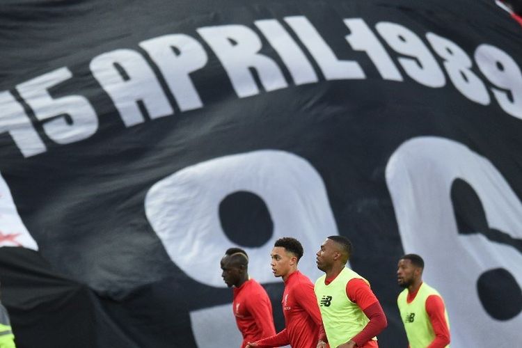 Para pemain Liverpool tengah melakukan pemanasan di hadapan suporter yang membentangkan spanduk terkait Tragedi Hillsborough jelang laga versus Huddersfield Town, 26 April 2019. 