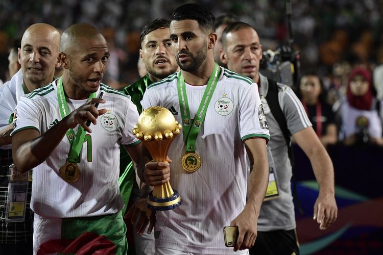 Penyerang sayap timnas Aljazair, Riyad Mahrez (kanan) dan Yacine Brahimi (kiri) mengangkat trofi setelah pertandingan final Piala Afrika (CAN) 2019 antara Senegal dan Aljazair di Stadion Internasional Kairo di Kairo pada 19 Juli 2019.