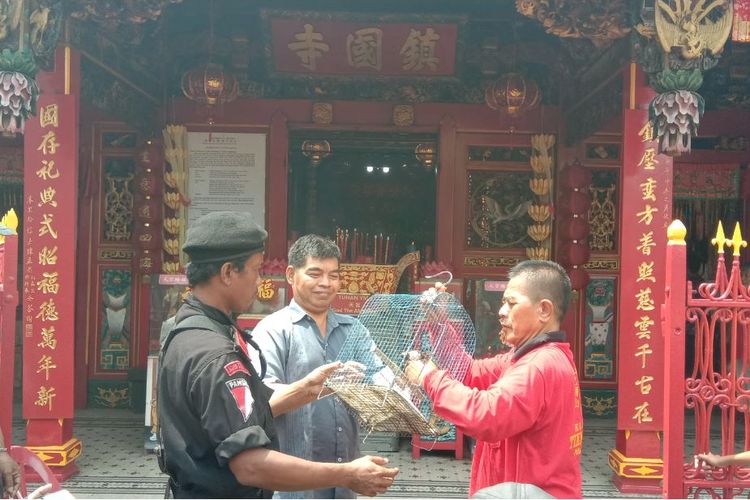 3 lelaki tengah melepaskan sejumlah burung pipit dari sangkarnya untuk tradisi Fang Sheng, di depan Klenteng Tien Kok Sie, Pasar Gede, Solo.