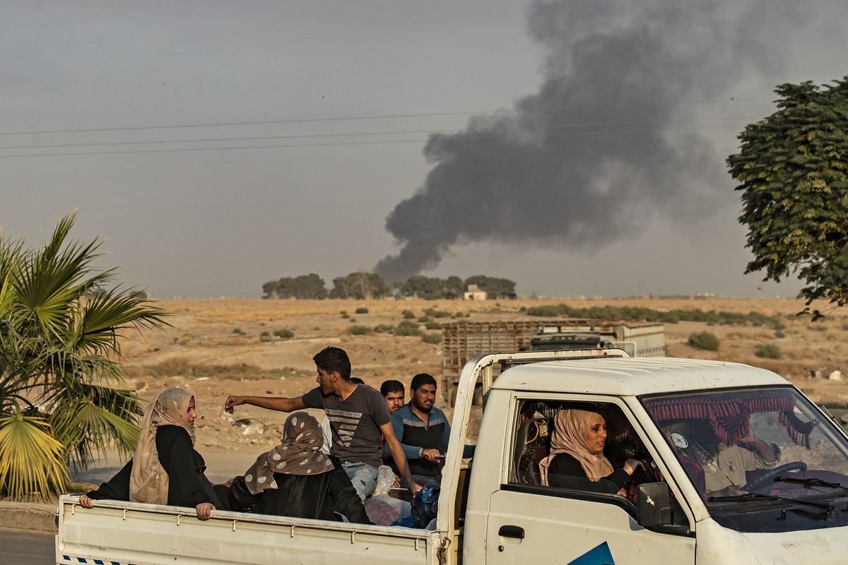 Sekelompok warga menaiki pikap melewati kota Ras al-Ain di Provinsi Hasakeh dengan asap mengepul buntut serangan Turki pada 9 Oktober 2019. Turku mengumumkan Operation Peace Spring untuk menghantam Kurdi Suriah yang mereka pandang sebagai teroris.