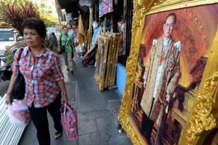 Seorang warga Bangkok berjalan melintas di depan lukisan besar Raja Bhumibol Adulyadej yang genap berusia 86 tahun pada Kamis (5/12/2013). Warga Thailand sangat menghormati sosok Raja Bhumibol, hingga para pengunjuk rasa antipemerintah berjanji untuk 