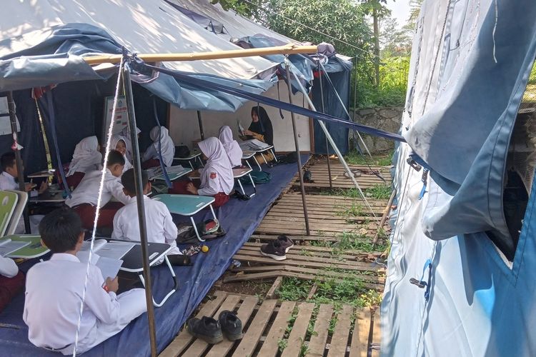 Murid SDN Cugenang, Kabupaten Cianjur, Jawa Barat ini masih belajar di tenda darurat, Senin (20/11/2023). Mereka terpaksa menjalani KBM dengan kondisi tak nyaman karena bangunan sekolah mereka yang rusak akibat gempa tahun lalu tak kunjung diperbaiki.