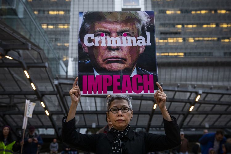 Connie Jeung-Mills dari San Francisco membawa poster menuntut pemakzulan dan pengunduran Presiden Amerika Serikat Donald Trump dalam sebuah reli di luar gedung federal di Seattle, Washington, Amerika Serikat, Selasa (17/12/2019). Donald Trump resmi menjadi presiden ketiga AS yang dimakzulkan setelah dalam sidang paripurna yang digelar 18 Desember malam waktu setempat, DPR AS menyetujui dua pasal pemakzulan terhadap presiden 73 tahun itu.