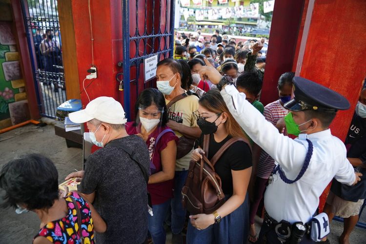 Orang-orang bergegas memasuki sekolah yang digunakan sebagai tempat pemungutan suara untuk memilih saat pembukaan pemilihan pada Senin 9 Mei 2022 di Kota Quezon, Filipina. 