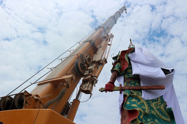 Petugas Badan Penanggulangan Bencana Daerah (BPBD) Pemkab Tuban, Jawa Timur, dengan menggunakan  alat berat crane menutup patung Dewa Perang Kongco Kwan Sing Tee Koen  dengan kain putih di Kelenteng Kwan Swie Bio, Minggu (6/8/2017). Patung setinggi 30,4 meter itu ditutup dengan kain oleh pengurus kelenteng karena adanya penolakan dari sejumlah elemen masyarakat atas patung itu. 