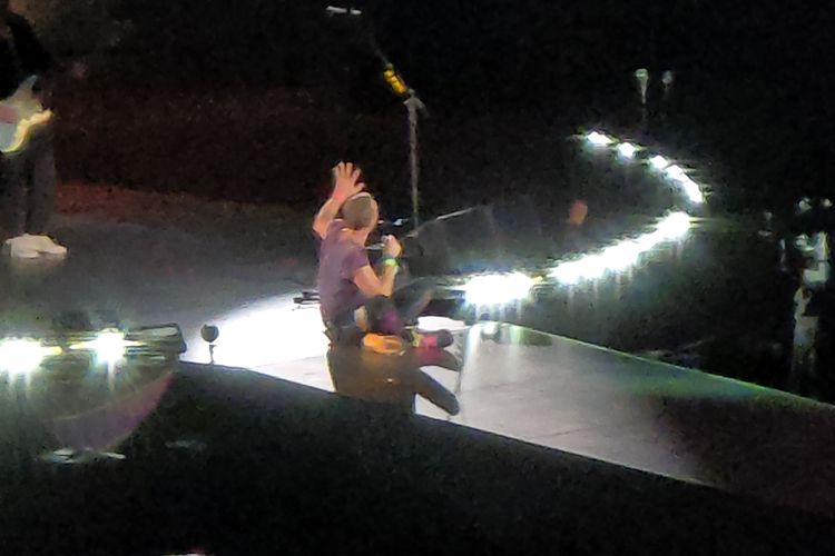 Vokalis band Coldplay, Chris Martin yang tengah duduk bersila di atas panggung sambil membawakan lagu berjudul Paradise