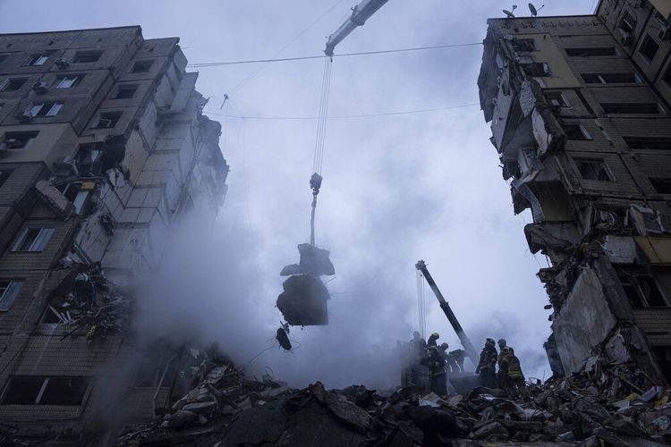 Petugas penyelamat menyisir puing-puing dari gedung apartemen yang hancur akibat serangan rudal Rusia di di Kota Dnipro, Ukraina, Minggu (15/1/2023).