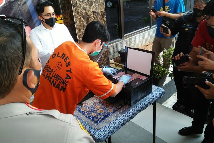 Tersangka pemalsuan uang palsu, M Javad (27) memeragakan cara dia mencetak uang palsu di Mapolresta Bandar Lampung, Senin (24/5/2020) sore. Tersangka membeli barang menggunakan uang palsu itu.