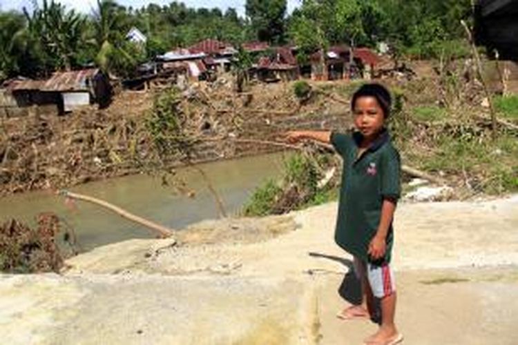 Brian (9), berdiri di atas lantai bekas rumahnya yang diterjang banjir bandang di Kelurahan Tikela, Minahasa, sambil menunjuk ke arah DAS Sawangan yang meluap waktu itu.