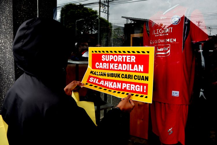 Seorang suporter Arema, Aremania menempelkan poster tuntutan saat melakukan aksi damai terkait Tragedi Kanjuruhan 1 Oktober lalu yang ditujukan kepada manajemen PT Arema Aremania Bersatu Berprestasi Indonesia di depan Store Arema FC Malang, Minggu (15/1/2023) siang.