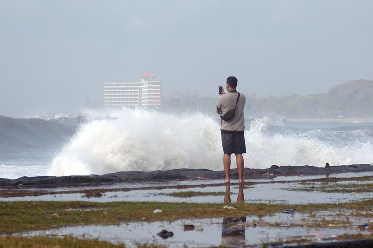 Warga menyaksikan gelombang tinggi di kawasan Pantai Padang Galak, Denpasar, Bali, Rabu (25/7/2018). Gelombang tinggi yang terjadi di Bali sejak seminggu terakhir mengakibatkan pelarangan aktivitas kapal cepat melalui Pantai Sanur dan Pelabuhan Padangbai serta merusak sejumlah pura di Bali.