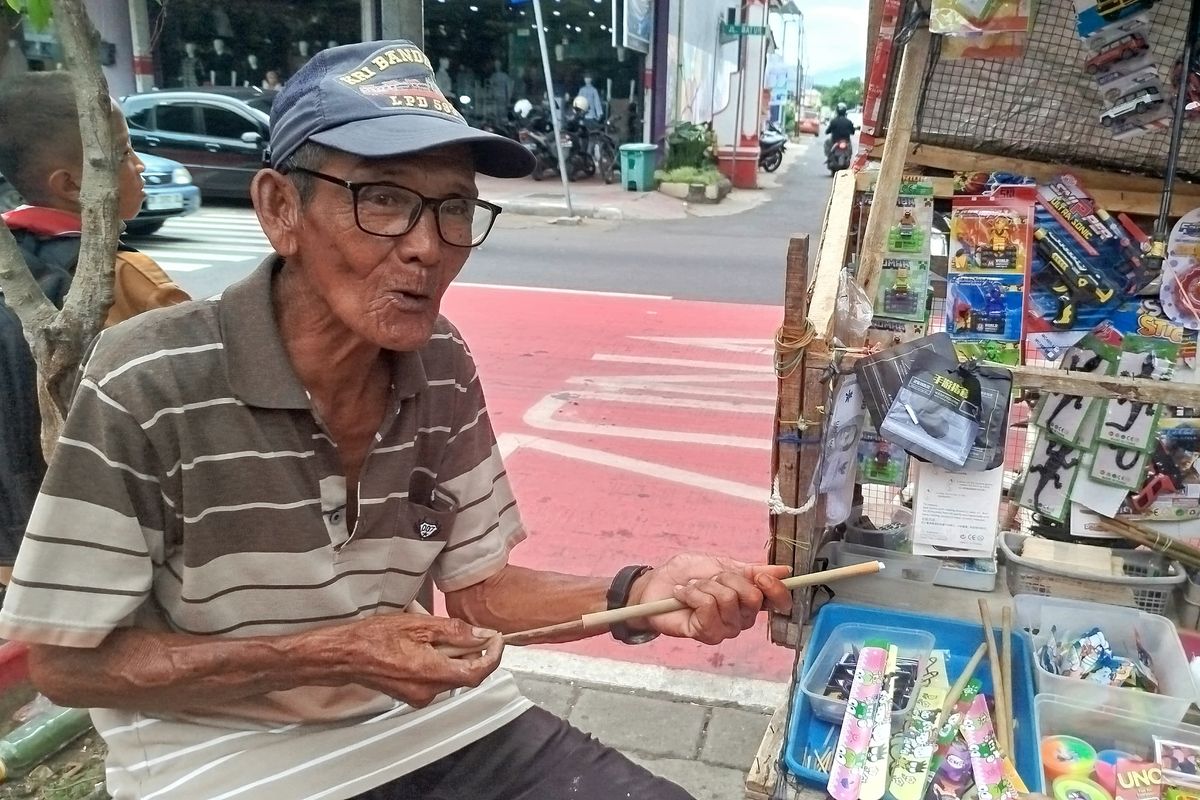 Ahmad mempraktekkan mainan tradisional tembak bambu yang dijualnya di depan SDN Lateng Banyuwangi, Sabtu (11/1/2025). 