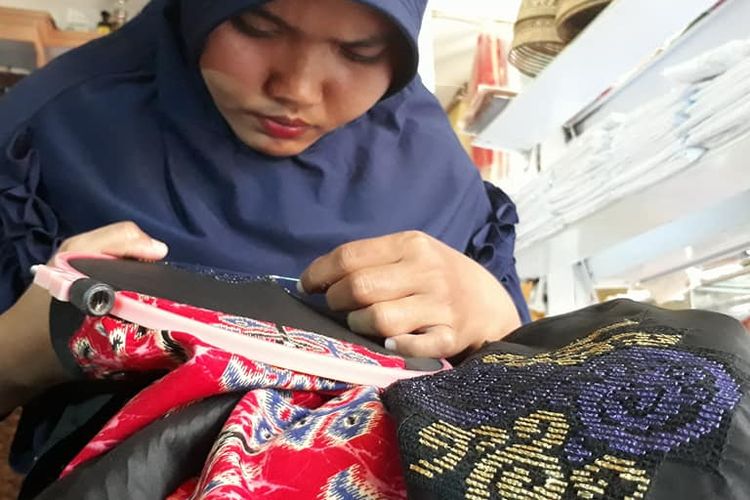 Seorang wanita membuat sulaman karawo, dimulai dengan mengiris serat benang kain hingga membentuk pola strimin, kemudian disulam sesuai pola yang ditetapkan.