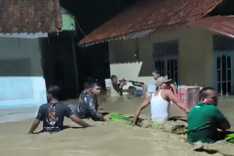 Warga Desa Ciuyah melintasi banjir yang merendam jalan utama desa dan juga rumah rumah warga pada Selasa (5/3/2024) malam.