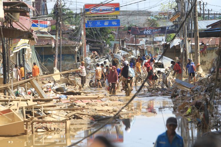 Sejumlah warga melintas di dekat puing-puing yang terbawa arus banjir di kawasan Desa Bukit Tempurung, Kota Kuala Simpang, Kabupaten Aceh Tamiang, Aceh, Rabu (3/12/2025). Menurut data Rabu, banjir dan tanah longsor di Sumatera menyebabkan 753 korban meninggal. BMKG jelaskan mengapa banyak korban, meski sudah ada peringatan dini.