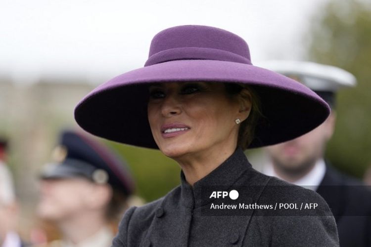 Melania Trump mengenakan topi ungu lebar dari Dior, yang dipadukan dengan setelan abu-abu gelap yang elegan.
