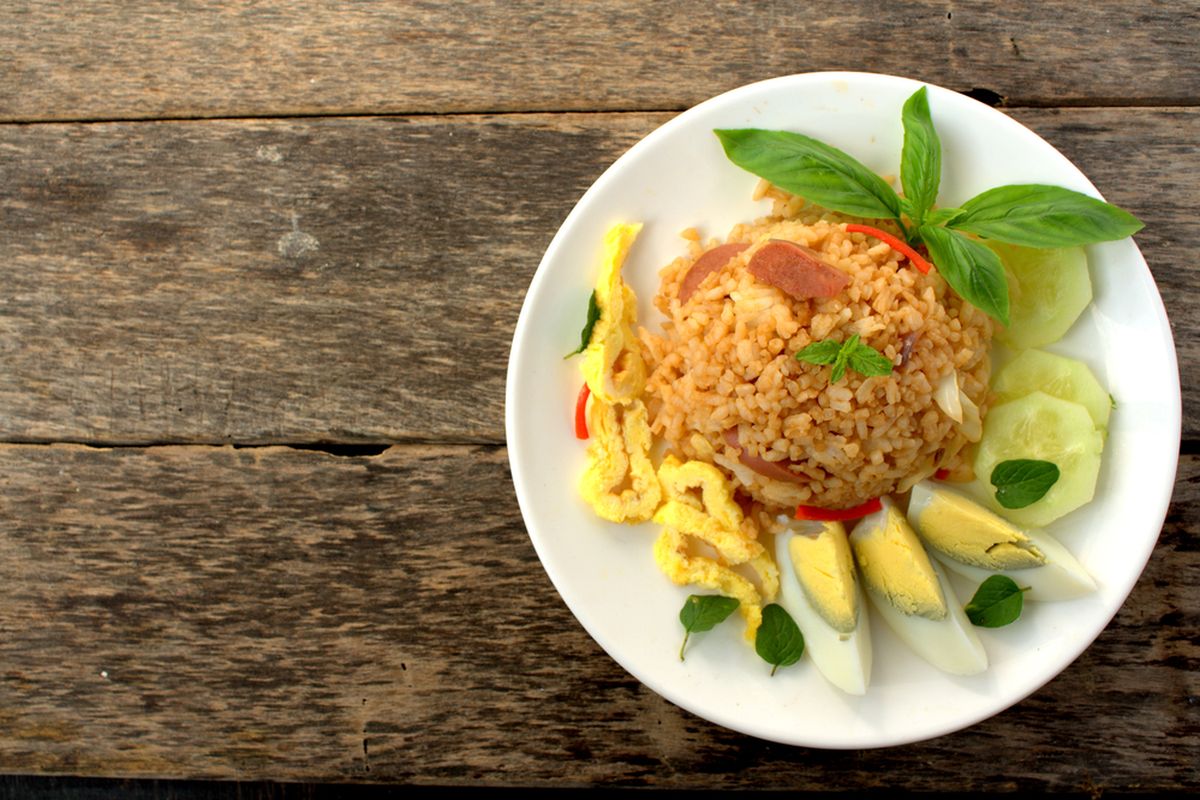 Ilustrasi nasi goreng dengan topping telur dadar, telur rebus, timun, dan daun kemangi. 