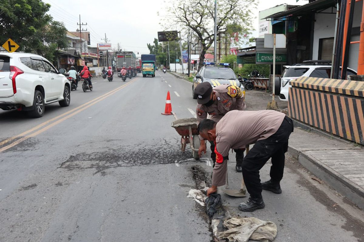 Kanit Binmas Polsek Manyar Aiptu Rozi dan Bripka Hadi Supriyanto, saat menambal jalan berlubang di jembatan Desa Sukomulyo, Kecamatan Manyar, Gresik, Jumat (4/2/2022).
