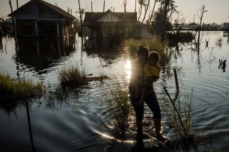 Seorang ibu membopong anaknya melewati banjir di rumahnya di Pekalongan 