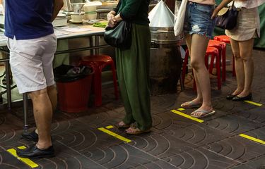 Terlihat garis-garis pembatas yang ditempel di perumukaan trotoar untuk membatasi jarak antar pembeli yang sedang mengantre membeli makanan di Yaowarat, Bangkok, Thailand