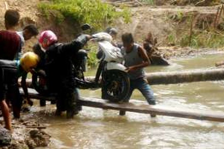 Pemuda Desa Wakalambe, Kecamatan Kapuntori, Kabupaten Buton, Sulawesi Tenggara, beramai-ramai mengangkat motor untuk melewati sungai akibat jembatan terputus