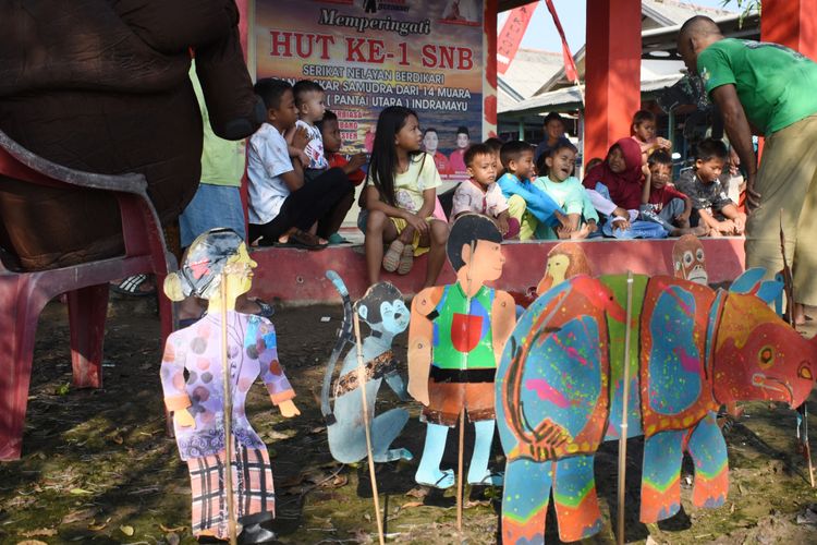 This picture taken on June 19, 2022 shows former teacher Samsudin (R) teaching children about animal conservation with cardboard puppets at Cemara Kulon village, in Indramayu. Samsudin is educating the young about the plight of the critically endangered Javan rhino - the world's rarest - with puppets on a stick, comical expressions and exaggerated voices, spreading his message of conservation one story at a time. TIMUR MATAHARI / AFP