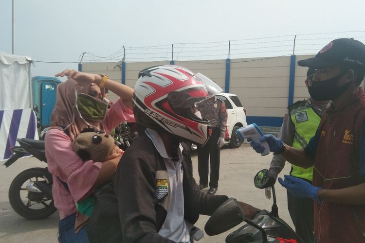 Petugas di titik check point Bundaran Kepuh, Jalan Lingkar Luar Karawang tengah memeriksa suhu tubuh pengendara, Jumat (14/5/2020).