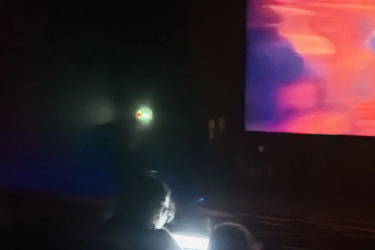 Seorang pengguna X membagikan gambar seorang pria yang sedang bekerja dengan laptop di dalam gedung bioskop di India.