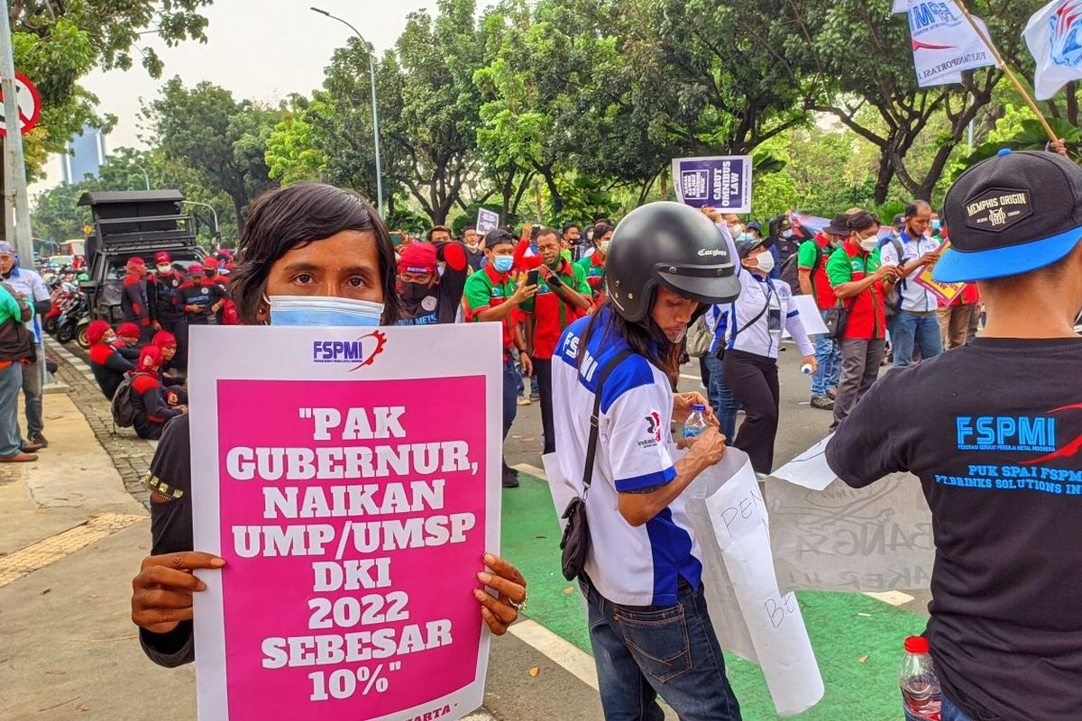 Seorang demonstran dari serikat buruh memegang poster tuntutan kenaikan UMP DKI 2022 sebesar 10 persen di depan Balai Kota DKI Jakarta, Selasa (26/10/2021)