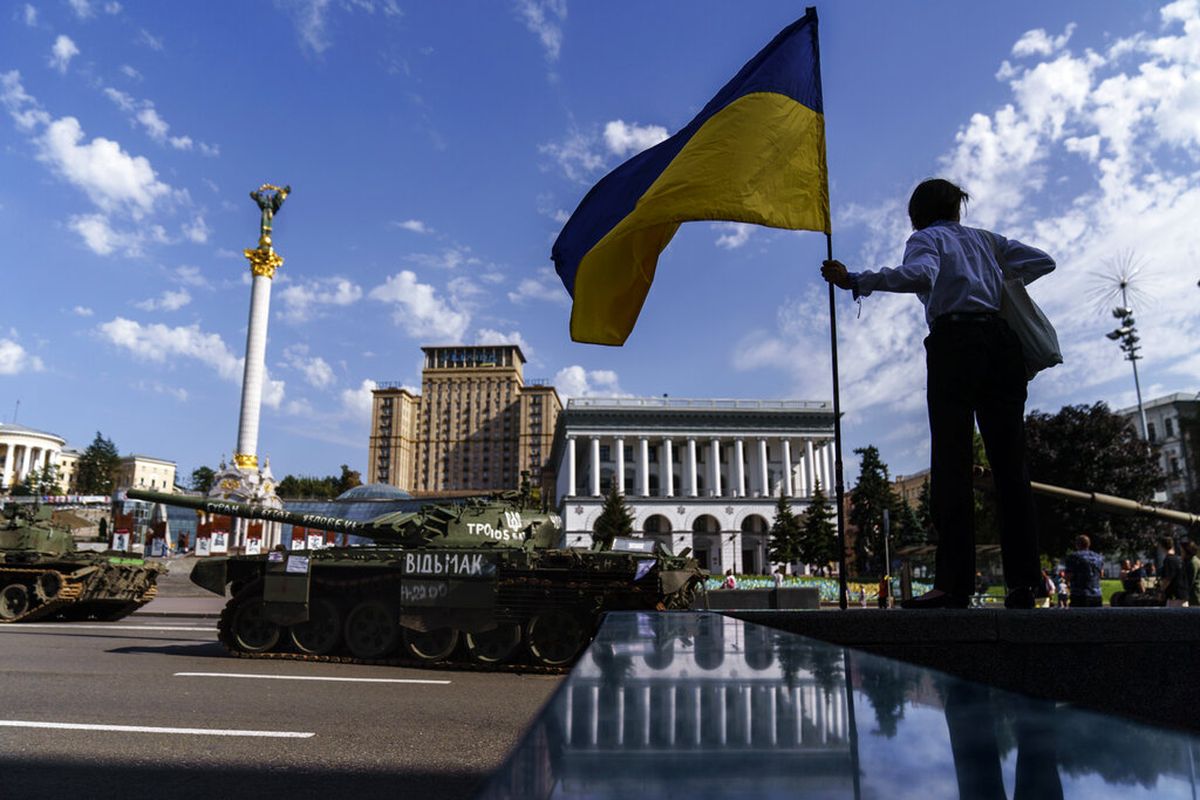 Seorang wanita memegang bendera Ukraina sambil melihat deretan kendaraan militer Rusia yang hancur yang dipajang di Maidan Square di Kyiv, Ukraina, Selasa, 23 Agustus 2022. 