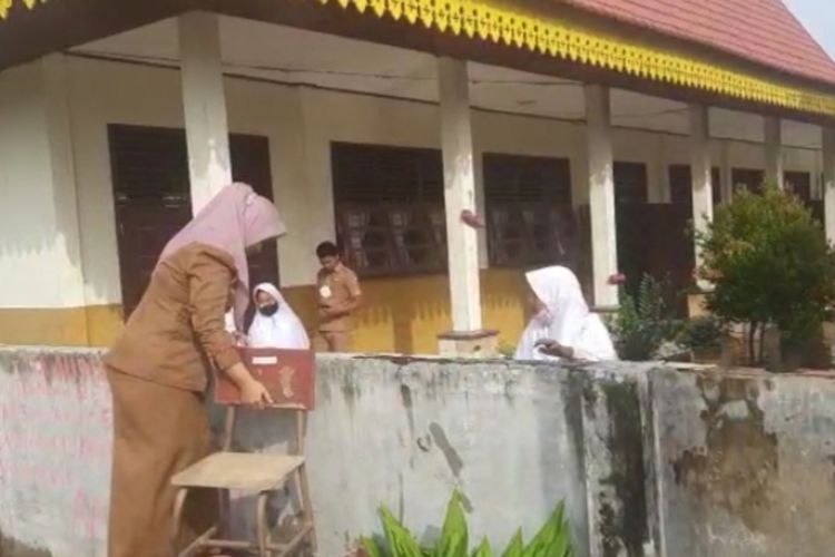 Seorang guru SDN 140 Pekanbaru memanjat pagar tembok untuk masuk ke sekolahnya akibat diterjang banjir, di Jalan Karya Bersama, Kelurahan Bambu Kuning, Kecamatan Tenayan Raya, Kota Pekanbaru, Riau, Senin (25/10/2021).