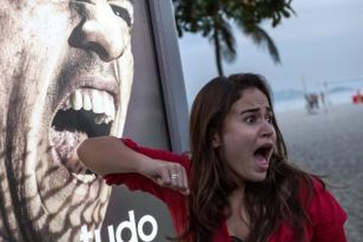 Seorang turis di pantai Copacabana, Rio de Janeiro, Brasil, Kamis 926/6/2014), berpura-pura takut di depan poster pemain Uruguay Luis Suarez yang seolah-olah menggigitnya.