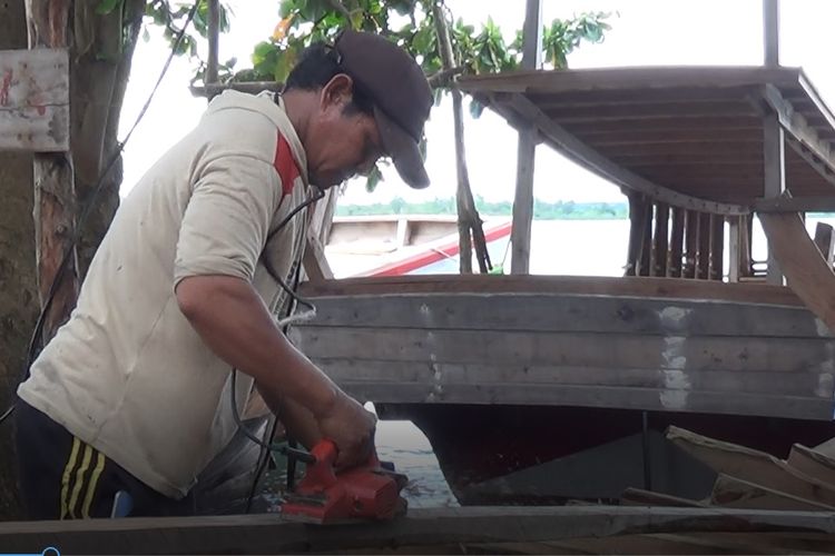 Ilham (42) sedang menggunakan mesin penghalus kayu dalam proses pembuatan kapal nelayan atau perahu pompong di Pulau Tinggi, Bangka Selatan, Sabtu (25/12/2021).