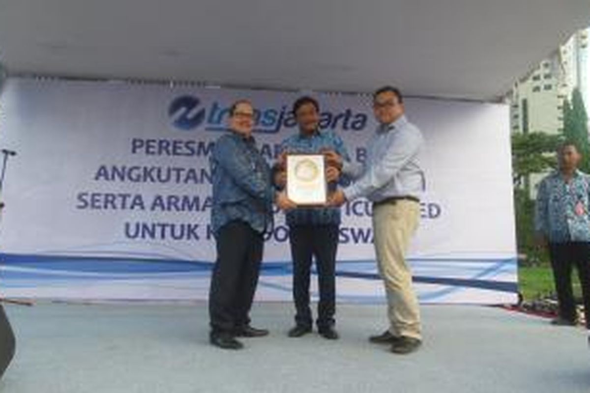 Direktur Institute for Transportation and Development Policy Indonesia, Yoga Adiwinarto (kanan) saat menyerahkan sertifikat bronze standard bus rapid transit (BRT) kepada Direktur Utama PT Transportasi Jakarta Antonius Kosasih (kiri) di Lapangan Parkir Timur, Senayan, Selasa (22/12/2015). Turut menyaksikan Wakil Gubernur Djarot Saiful Hidayat (tengah). Sertifikat diberikan untuk penilaian ITDP yang menganggap ada enam koridor layanan bus transjakarta sudah berstandar sistem BRT internasional.