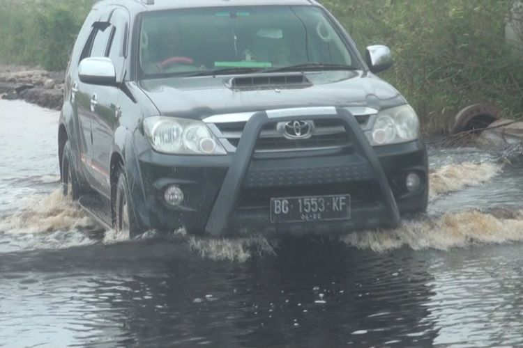 Sebuah kendaraan nekad melitasi banjir meksi dengan resiko mesinnya terendam banjir.