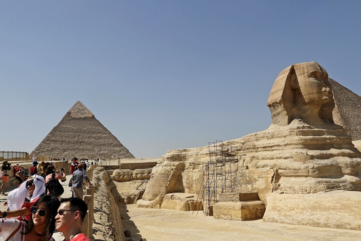 Wisatawan berfoto dengan latar belakang patung Spink dan piramida di Mesir.