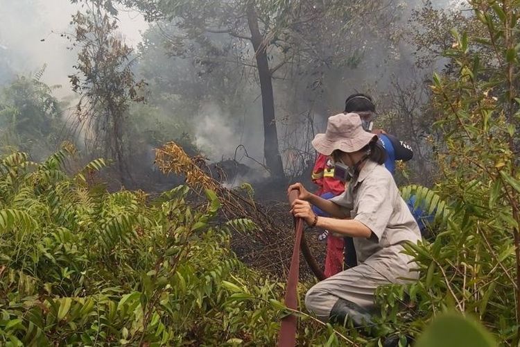 Sumarni (kiri) menarik selang untuk melancarkan aliran air dalam upaya pemadaman salah satu titik api di Palangkaraya, Kalimantan Tengah (18/09) 