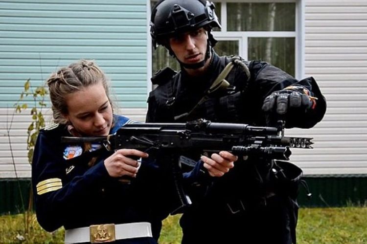 Seorang prajurit Rusia tengah melatih seorang remaja perempuan mengoperasikan senapan serbu.