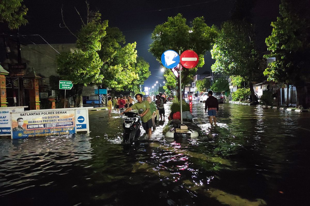 Pemotor mendorong sepeda motor yang mogok dampak banjir di Jalan Sultan Fatah Demak, Senin (18/3/2024) malam. 