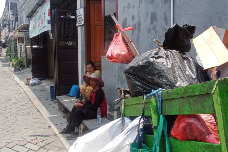 Pak Markan sedang beristirahat di pinggir jalan Gang 1 Lidah Wetan sambil berteduh dan berbincang dengan warga sekitar yang memberikannya minuman dan kopi hitam.