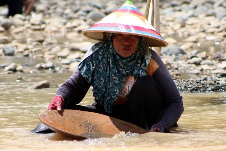Seorang wanita mendulang emas di tepi Sungai Paguyaman Gorontalo. Kandungan emas di batuan ini memberi harapan bagi para warga untuk mendulang di manapun.