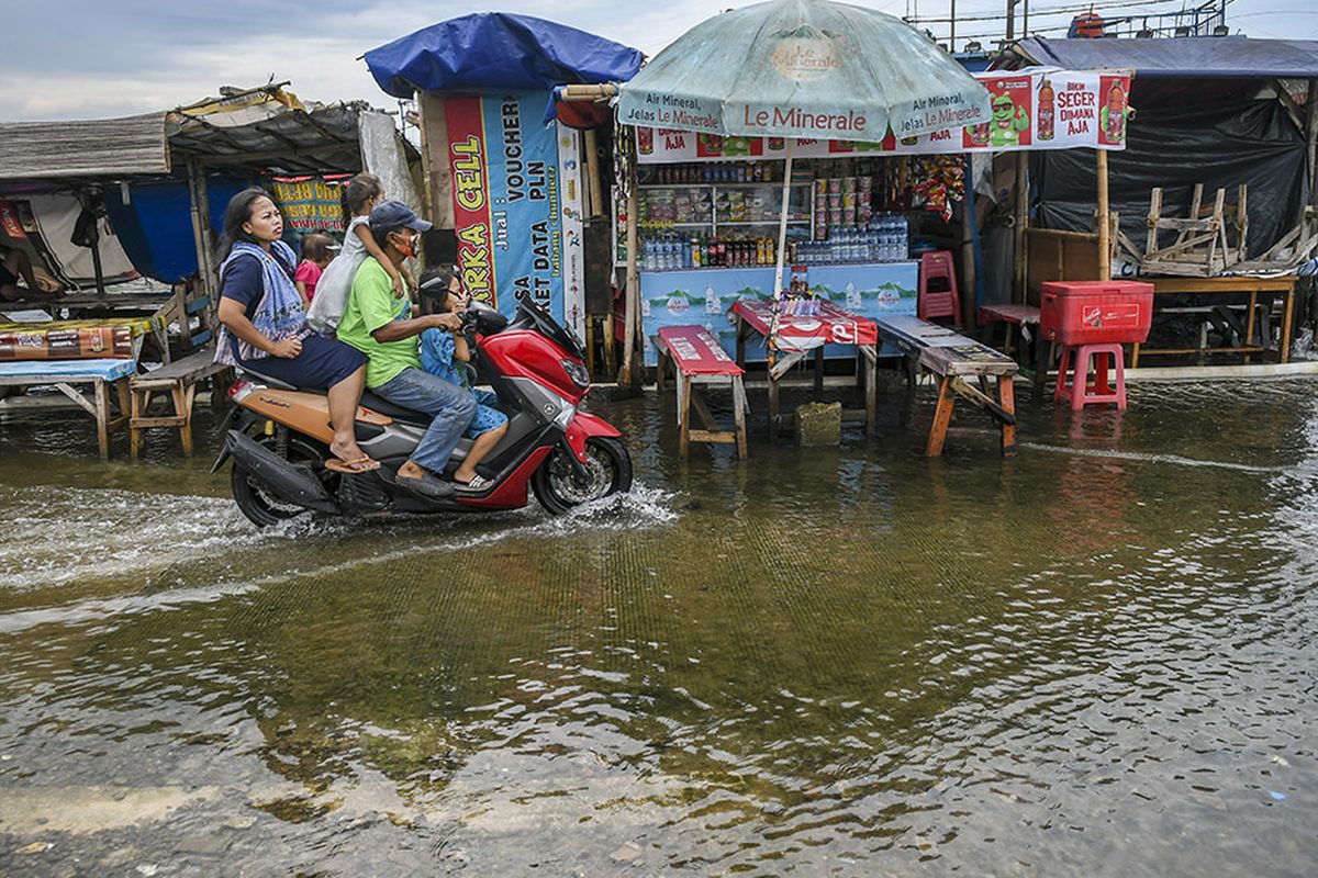 Warga menaiki motor melintasi banjir rob di Pelabuhan Kali Adem, Muara Angke, Jakarta, Jumat (1/1/2021). Banjir yang terjadi sejak Kamis (31/12/2020) itu dikarenakan pasang surut air laut.