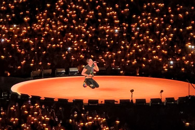 Vokalis Coldplay, Chris Martin yang sedang berlutut sambil bernyanyi di atas panggung konse Coldplay bertajuk Coldplay Music of the Spheres World Tour