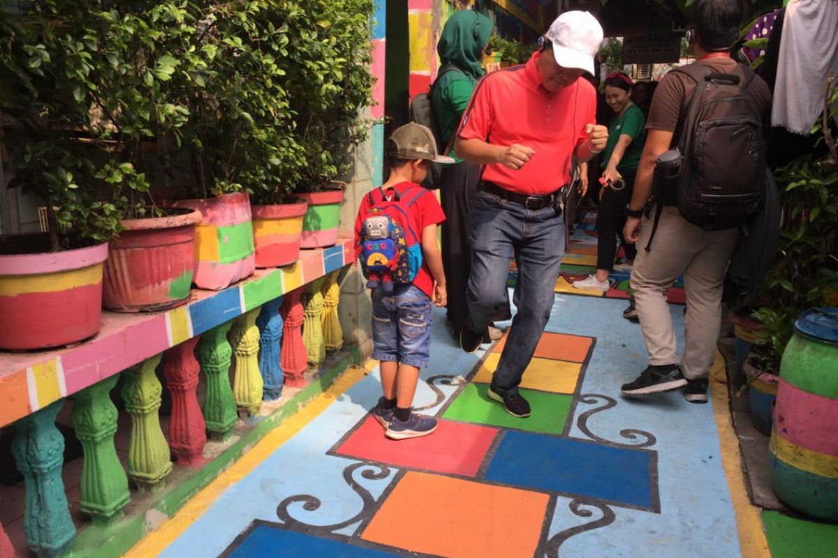 Asisten Pembangunan dan Lingkungan Hidup Pemprov DKI Yusmada Faizal menjajal permainan engklek pada mural yang digambar di atas jalan perkampungan ramah pejalan kaki di Sunter Jaya, Minggu (4/11/2018).