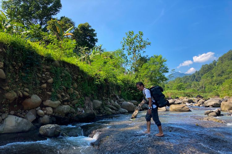 Seorang wisatawan sedang menyeberangi aliran sungai di Kecamatan Babakan Madang, Kabupaten Bogor, Rabu (26/5/2021).