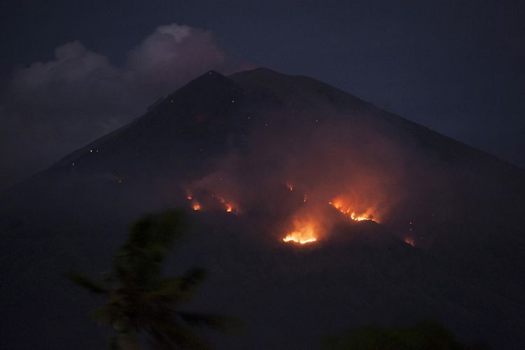 Api membakar hutan lereng Gunung Agung setelah terjadinya lontaran batu pijar dari kawah, terlihat dari Desa Culik, Karangasem, Bali, Selasa (3/7/2018). Pusat Vulkanologi dan Mitigasi Bencana Geologi mencatat terjadinya erupsi Gunung Agung dengan tinggi kolom abu mencapai 2.000 meter yang disertai lontaran batu pijar sejauh dua kilometer.