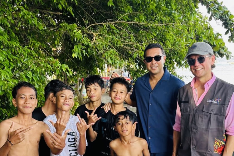 Asisten pelatih timnas Indonesia Alex Pastoor dan Denny Landzaat foto bersama anak-anak yang menikmati kelapa muda di Pantai Jikomalamo dengan keindahan air laut yang begitu jernih dengan gradasi warna biru kehijauan, Senin (10/2/2025) siang.