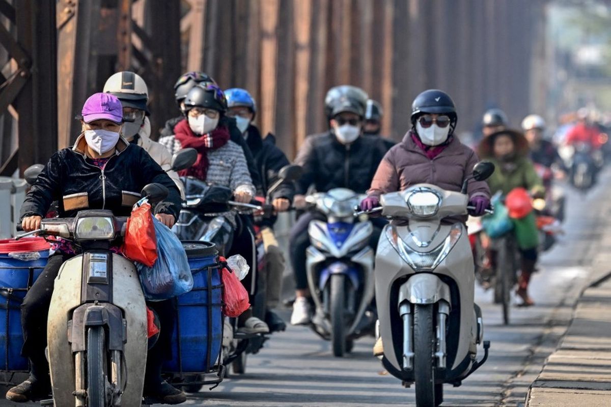 Pengemudi yang mengenakan masker wajah mengendarai skuter di sepanjang Jembatan Long Bien di tengah polusi udara yang parah di Hanoi pada 3 Januari 2025. Kabut asap tebal menyelimuti Hanoi pada 3 Januari, mengaburkan bangunan-bangunan dan menyebabkan sembilan juta penduduk tercekik oleh udara beracun saat ibu kota Vietnam tersebut menduduki puncak daftar kota-kota besar paling tercemar di dunia.